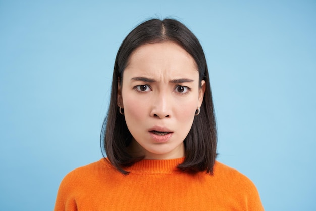 Close up portrait of asian girl with shocked face looks at smth unbelievable startled by news stands