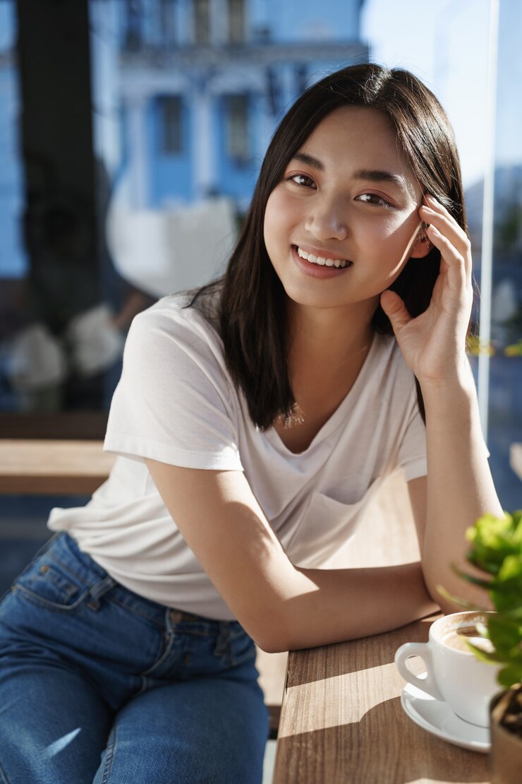무료 Photo 창 근처 레스토랑에 앉아서 커피를 마시는 아시아 여자의 초상화를 닫습니다.