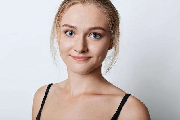 Close up portrait of attractive female with freckled skin, blue eyes and dimples on cheeks, having confident look into camera, isolated on white. Cute blonde female posing in studio