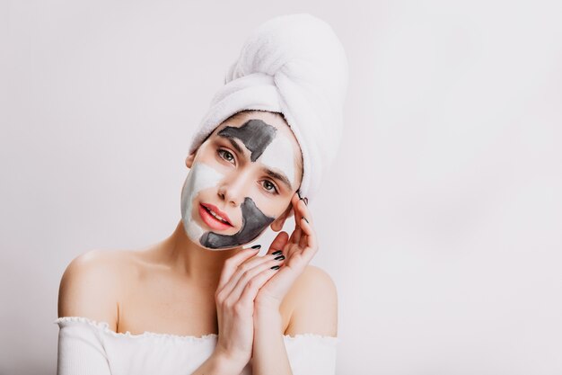 Макро портрет привлекательной девушки делать лицевую маску перед сном. Взрослая женщина позирует на белой стене.