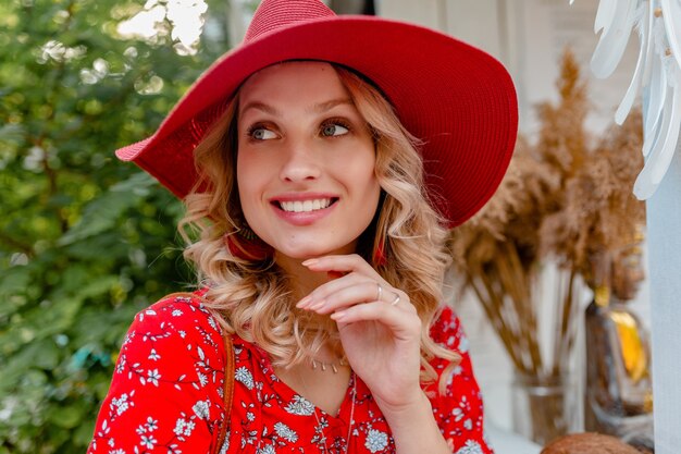 わらの赤い帽子と笑顔でブラウスの夏のファッション衣装で魅力的なスタイリッシュな金髪の笑顔の女性のクローズアップの肖像画