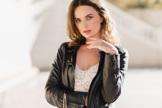 Close up portrait of attractive woman walking in street in fashionable outfit, wearing black leather jacket and white lace dress, spring autumn style