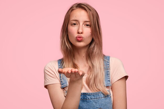 Close up portrait of attractive young Caucasian female blows air kiss at camera as flirts with her boyfriend