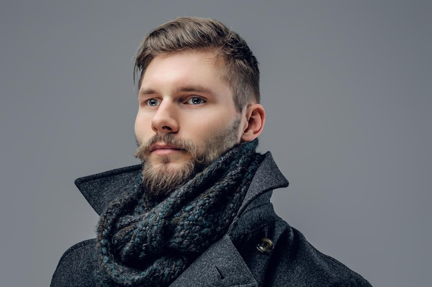 Close up portrait of bearded male dressed in a warm jacket and a scarf isolated on grey background.