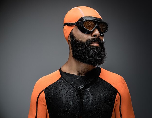 Close up portrait of bearded male in scuba diving mask and orange neopren diving suit isolated on grey background.