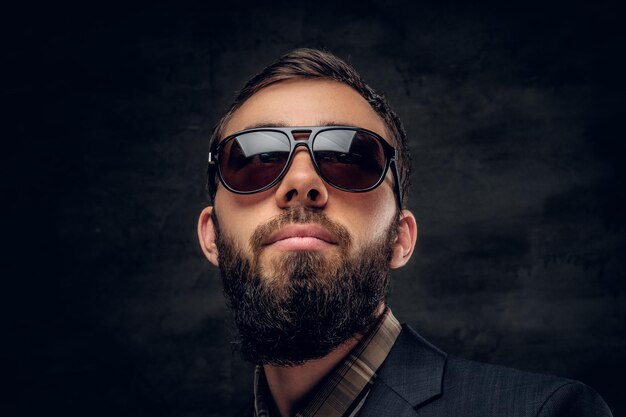 Close up portrait of bearded male in sunglasses isolated on grey vignette background.