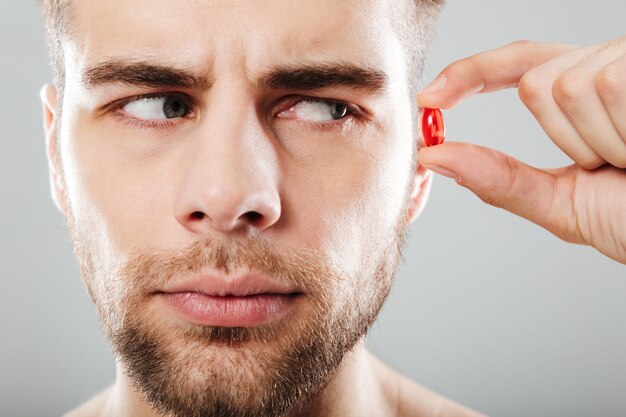 close up portrait of a bearded man holding red capsule