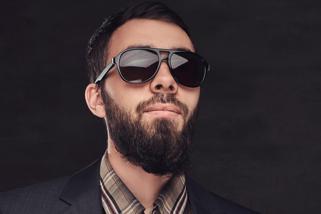 Close-up portrait of a bearded man wearing a suit and sunglasses. Isolated on a dark background.