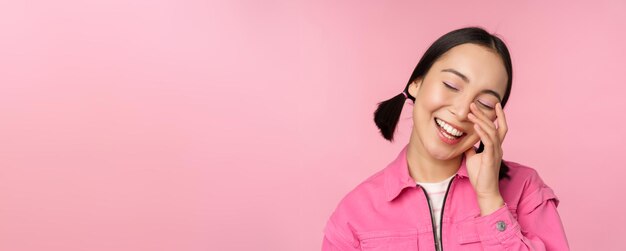 분홍색 배경에 서서 행복하게 웃고 열정적으로 웃고 웃고 있는 아름다운 아시아 소녀의 초상화를 클로즈업