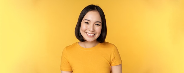 노란색 b에 대해 귀엽고 부드러운 서 있는 미소를 짓고 있는 아름다운 아시아 여성의 초상화를 클로즈업