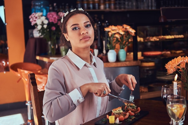 Close-up portrait of a beautiful black-skinned woman wearing a blouse and flower headband, enjoying dinner while eating in a restaurant.