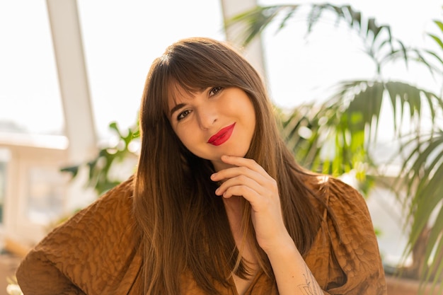 Close up portrait of beautiful brunette woman posing in stylish bohemian living room with home plants