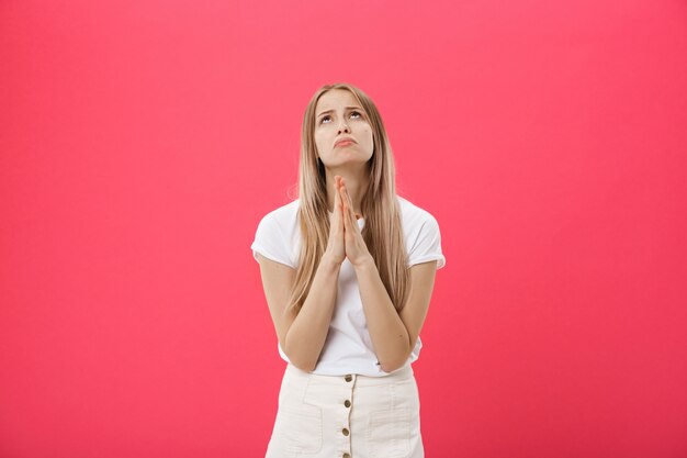 Close up portrait of beautiful caucasian teenage girl praying isolated against pink background