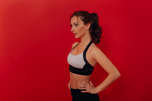 Close up portrait of beautiful dark-haired woman wearing sport top isolated on red wall