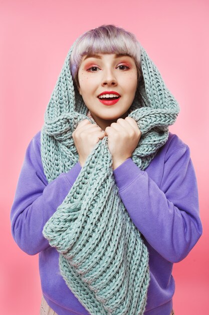 Close-up portrait of beautiful dollish girl with short light violet hair wearing lilac sweater and grey knitted neckwarmer over pink wall