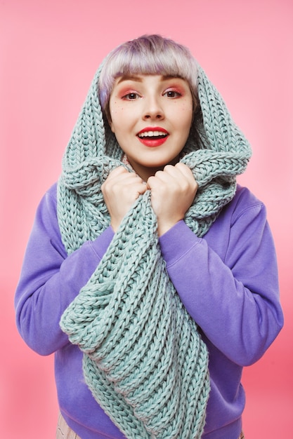 Close-up portrait of beautiful dollish girl with short light violet hair wearing lilac sweater and grey knitted neckwarmer over pink wall