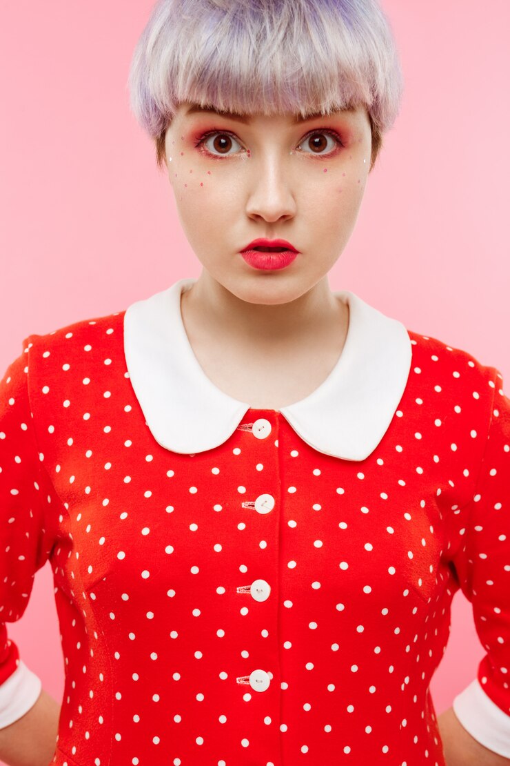 무료 Photo 분홍색 벽에 빨간 드레스를 입고 짧은 밝은 보라색 머리를 가진 아름다운 인형 소녀의 초상화를 닫습니다
