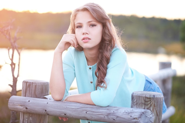 Free photo close-up portrait of a beautiful girl, standing outdoors while leaning on a wooden fence.