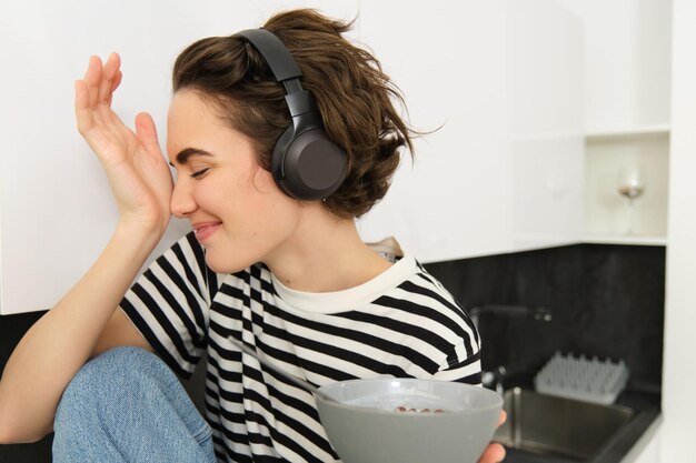 Close up portrait of beautiful happy woman listens music in headphones and eats cereals for