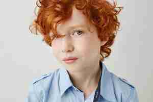 Free photo close up portrait of beautiful little kid with red curly hair and grey eyes looking with serious and relaxed expression.