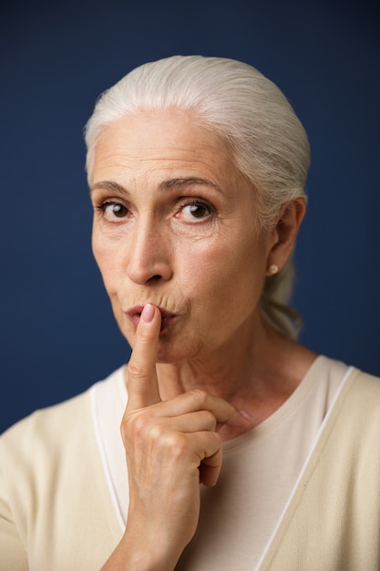Close-up portrait of beautiful old woman, showing silence gesture