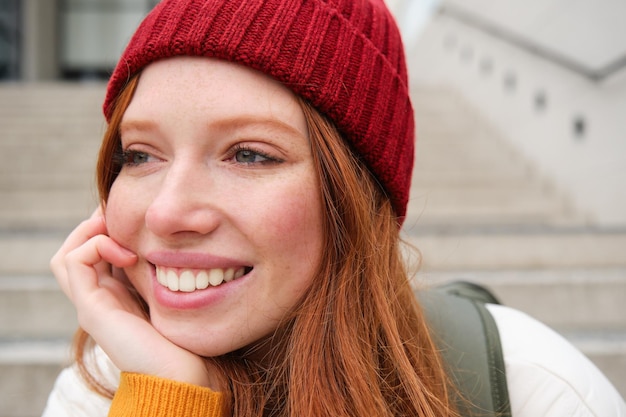 Close up portrait of beautiful redhead girl in red hat urban woman with freckles and ginger hair sit