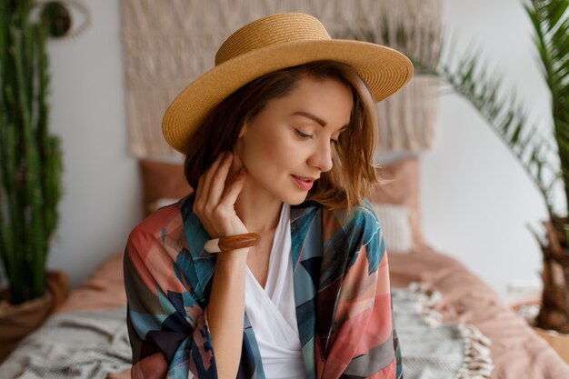 Close up portrait of beautiful romantic woman in straw hat chilling over bohemian interior