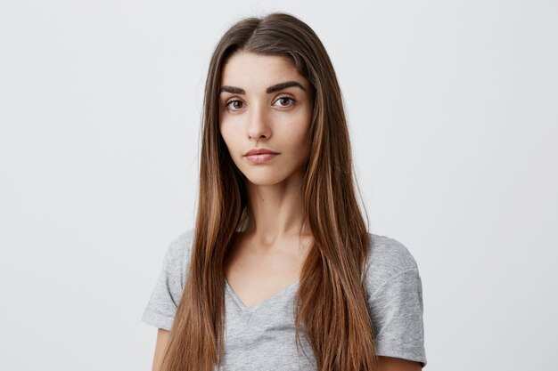 Close up portrait of beautiful serious dark-haired caucasian woman with long hairstyle in casual gray shirt  with relaxed and calm face expression. Health and beauty.