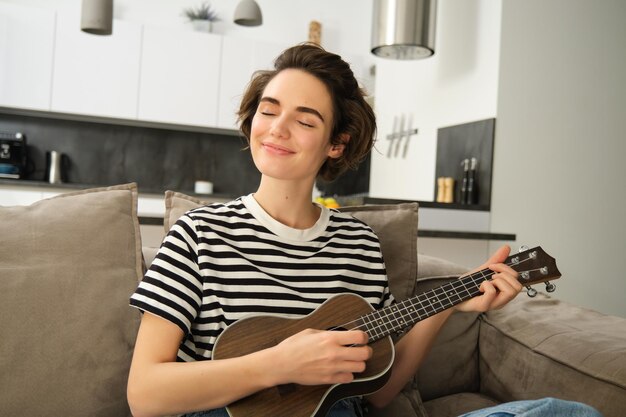 Ritratto ravvicinato di una bella donna sorridente che suona l'ukulele strimpellando le corde con gli occhi chiusi e