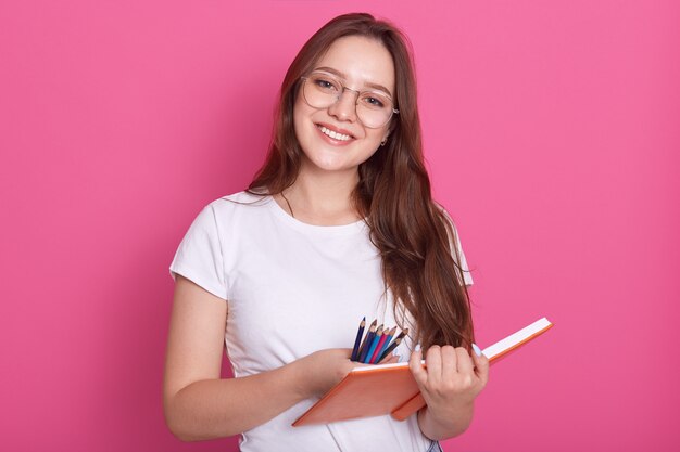 Close up portrait of beautiful student girl ready to make notes in copybook, having pleasant look