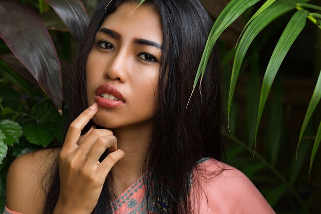 Close up portrait of beautiful thai woman over tropical leaves. Spa and relax concept.