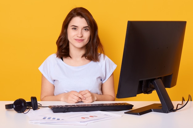 Close up portrait of beautiful young brunette female sitting at white desk in front of computer at home