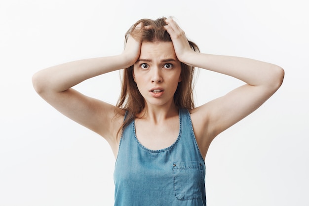 Free photo close up portrait of beautiful young dark-haired european woman in casual blue t-shirt squeezing forehead with hands,  with confused and lost face expression.
