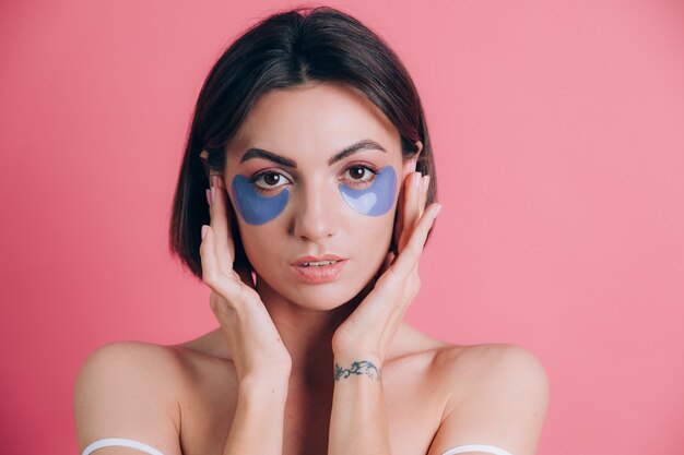 Close-up portrait of a beautiful young woman topless open shoulders with blue collagen pads under her eyes. Beauty concept.