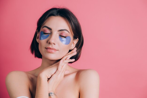 Close-up portrait of a beautiful young woman topless open shoulders with blue collagen pads under her eyes. Beauty concept.