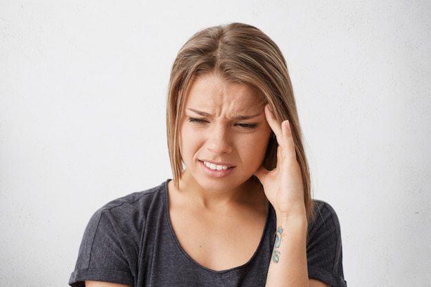 Close up portrait of beautiful young woman with bob hairstyle holding hand on her temple, writhing in pain as her head aching, feeling sick and stressed. Headache, migraine, sickness and illness