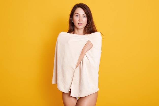 Close up portrait of beautiful young woman with dark staright hair posing wrapped fresh white bath towel