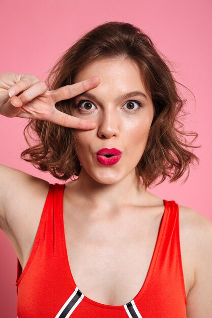 Close-up portrait of beautiful young woman with red lips showing peace gesture, 