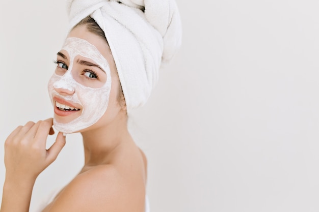 入浴後タオルで美しい若い女性のクローズアップの肖像画は、彼女の顔に化粧品のマスクを作ります。