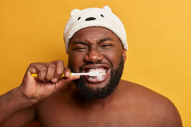 Close up portrait of black Afro man brushes teeth, has daily morning routine