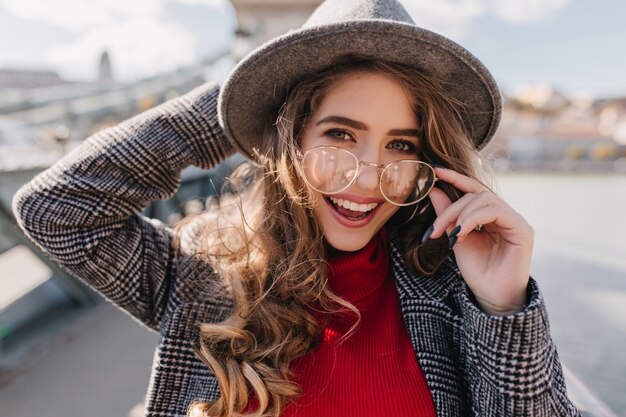 Close-up portrait of blissful blue-eyed girl touching glasses and laughing