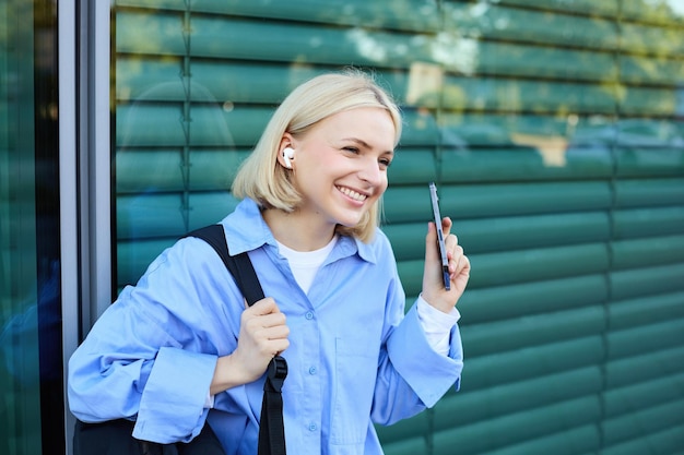 Close up portrait of blond smiling female model college student in earphones listening to music on