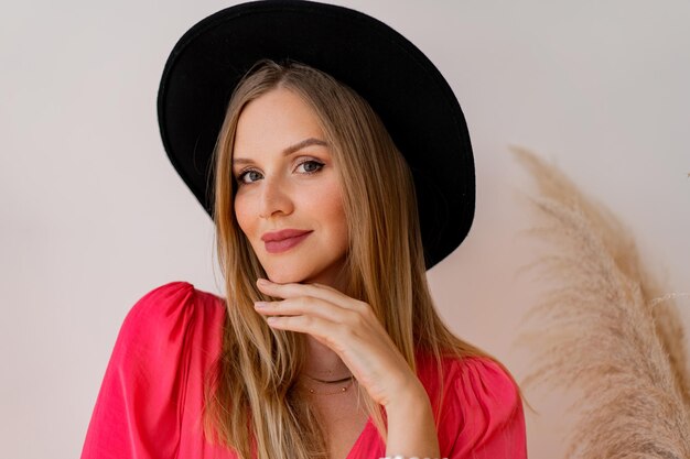 Close up  portrait   blond woman in black hat and ink dress posing in studio  in studio with pampas grass decor