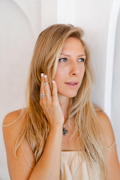 Close up portrait of blond woman in casual outfit posing over stylish beige interior Accsessorises tropical mood vacation time