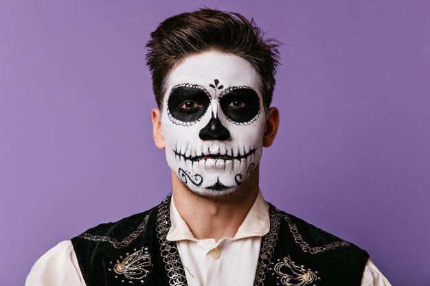 Close-up portrait of brunet with face painted for Halloween. Brown-eyed guy in white shirt