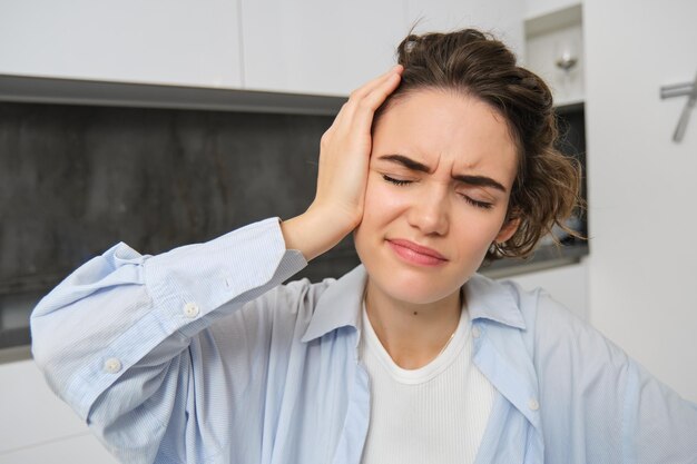 Close up portrait of brunette woman touches her head feels dizzy has migraine or headache grimaces f