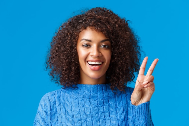 Close-up portrait carefree, happy joyful woman celebrating holidays, wishing everyone good new year, showing peace sign and smiling joyfully, express posivity and joy, wearing sweater.