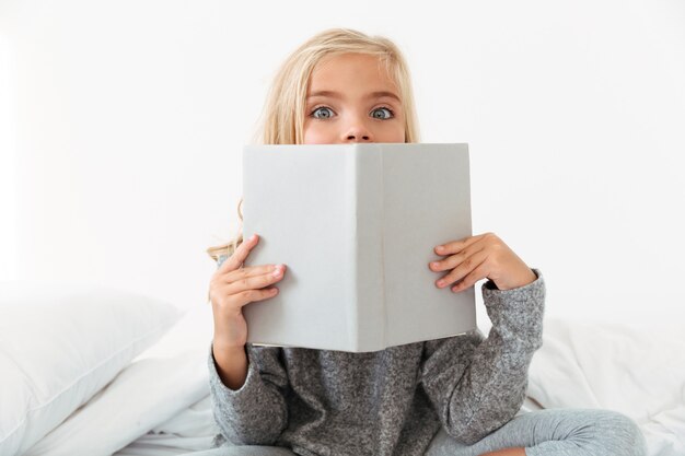 Close-up portrait of charming girl covering her face with book, 