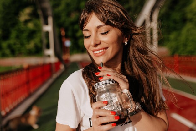 Close up portrait of charming girl with wonderful wide smile enjoying morning coffee with closed eyes in sunlight