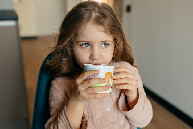 Close up portrait of charming lovely little girl is drinking tea at home in the morning Lovely girl at the kitchen is having great time